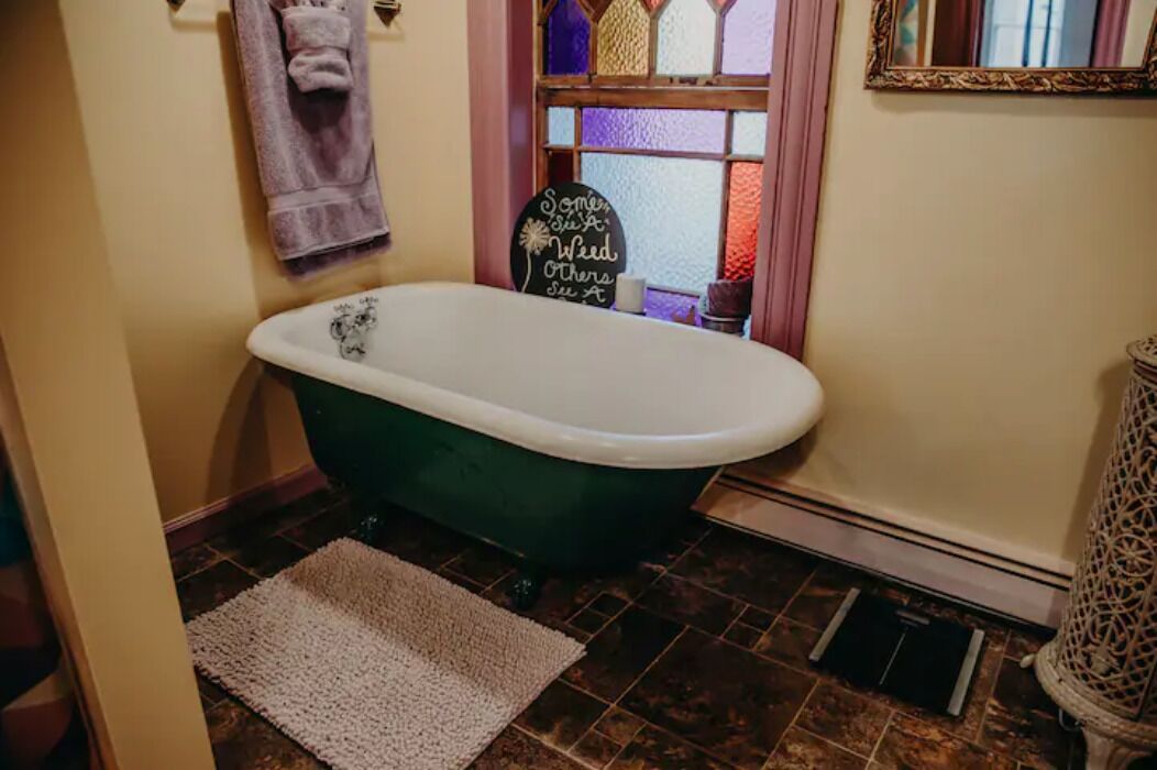Een badkamer met een badkuip op poten in groene tinten, een witte wastafel en een decoratief bord aan de muur.