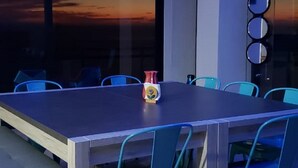 Een moderne vergaderruimte met een lange tafel en blauwe stoelen, een groot raam met uitzicht op een zonsondergang, en een decoratieve spiegel aan de muur.