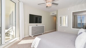Een slaapkamer met een groot bed, een flatscreen televisie, een plafondventilator en uitzicht door een schuifdeur.
