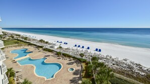 Een resort met een groot zwembad, een zandstrand en een helderblauwe lucht.