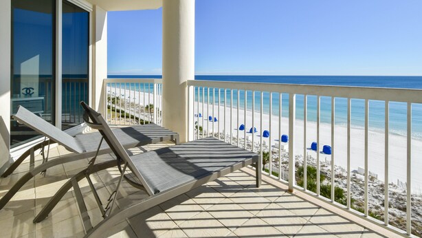 Een balkon met ligbedden met uitzicht op een strand.