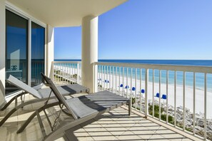 Een balkon met ligbedden met uitzicht op een strand.