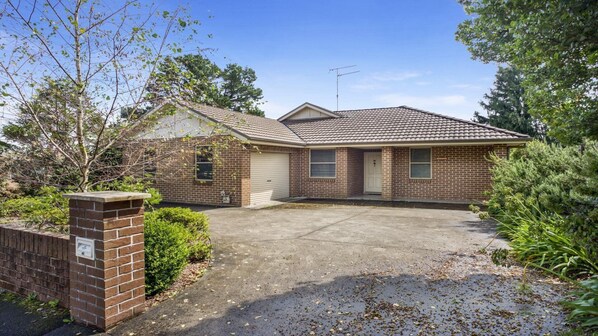 A single-story brick house with a tiled roof, a front garage, and a driveway leading to the entrance.