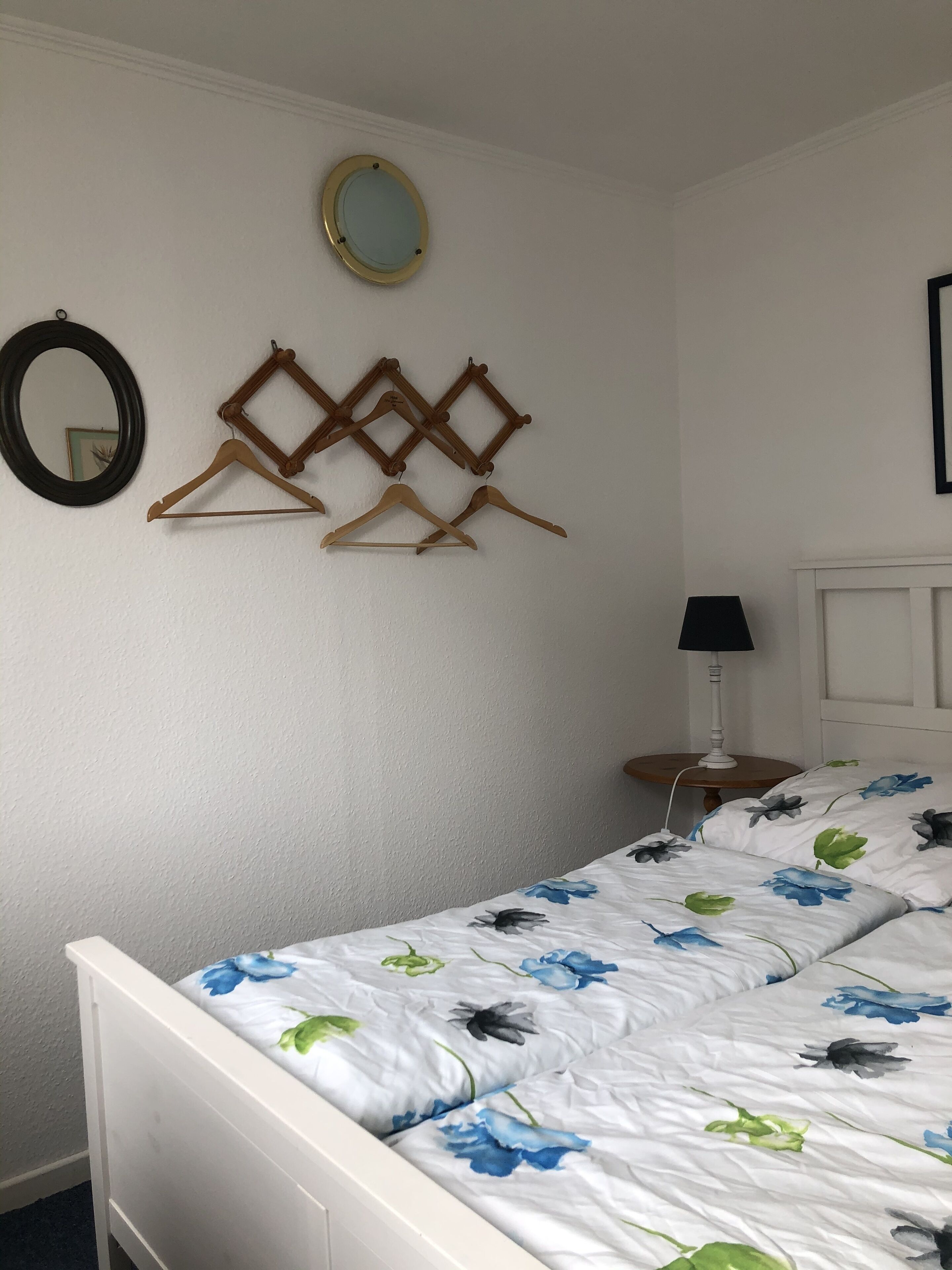 A bedroom with a bed, a mirror, and wooden hangers on the wall.