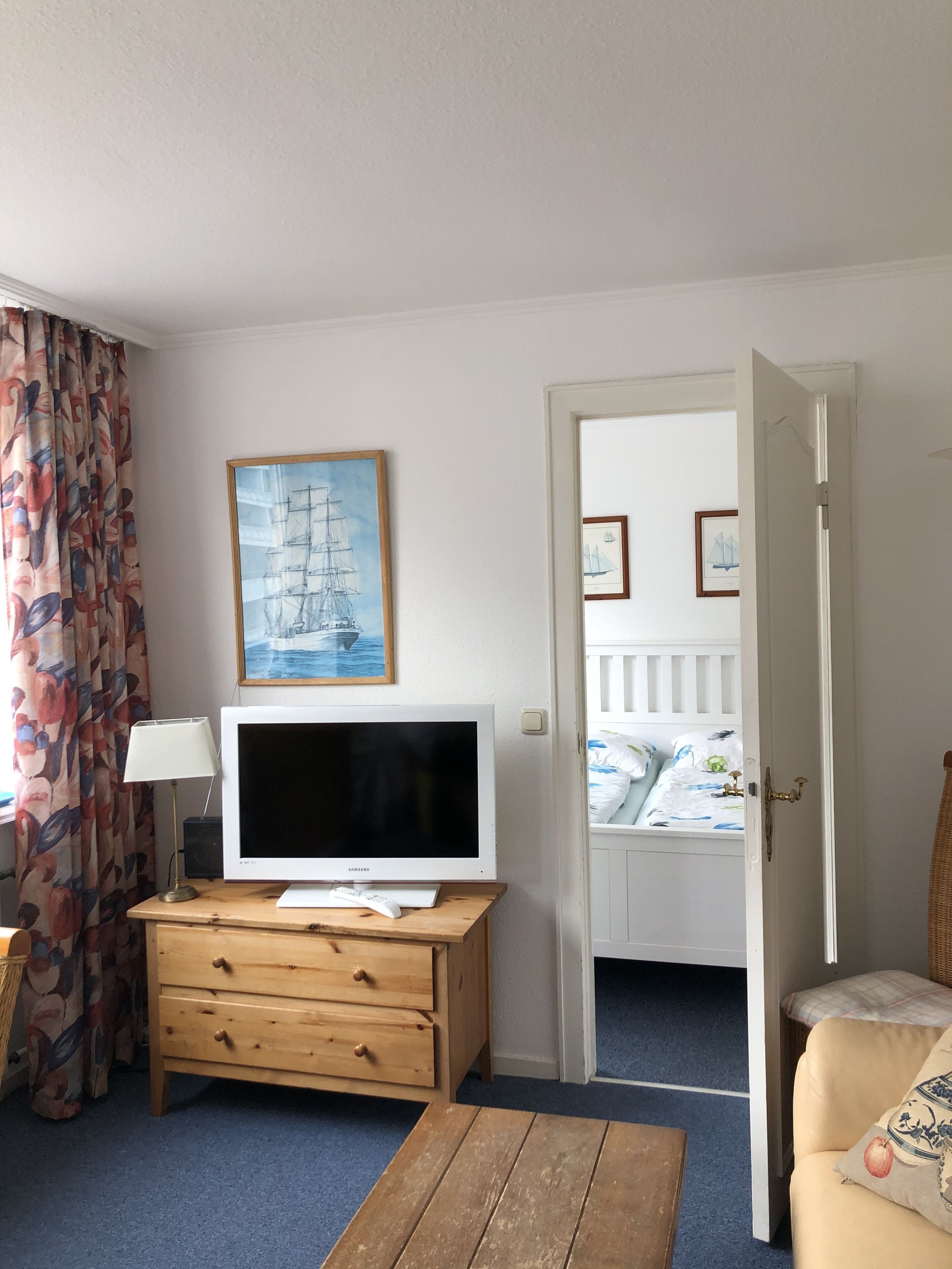 A room with a wooden dresser, a flat-screen TV, a lamp, and a bed with a white headboard.