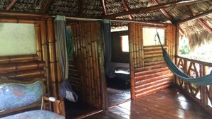 Une hutte en bambou avec un toit de chaume, un hamac et un lit muni d’une moustiquaire.