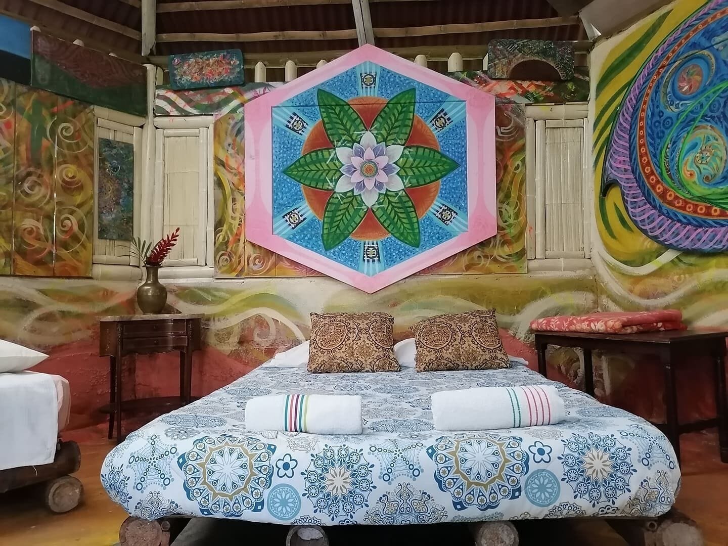 Una habitación con una cama, almohadas, un florero y un mural de pared colorido.
