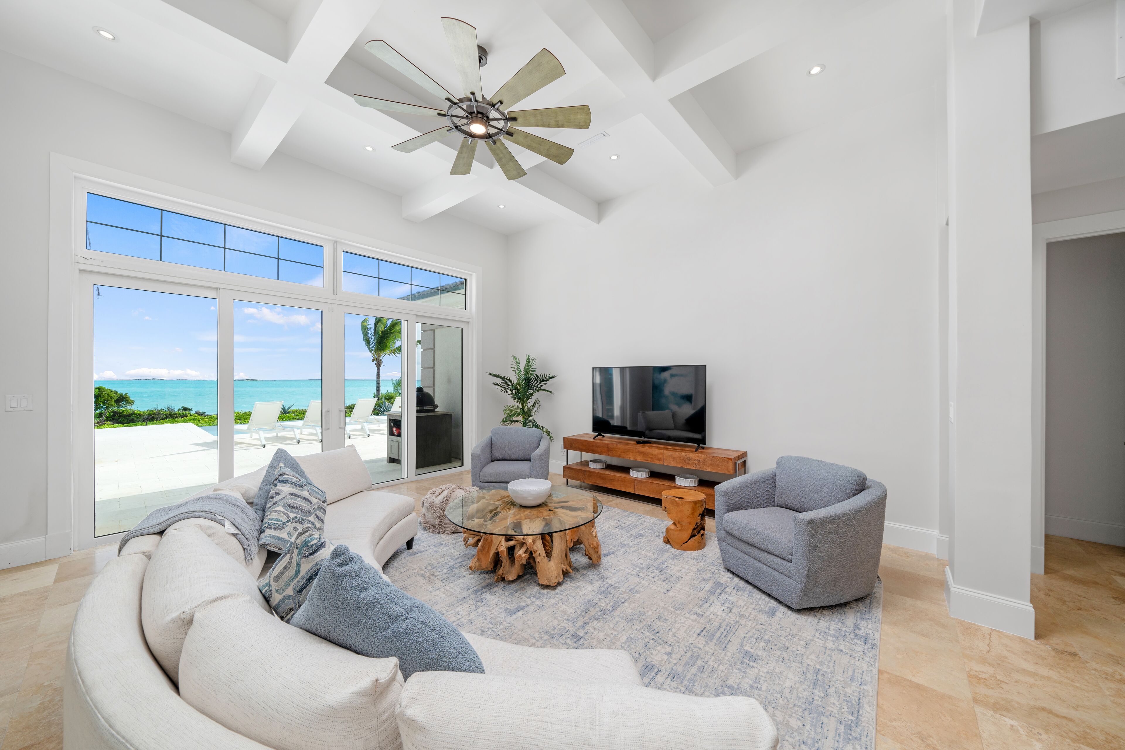 A spacious living room with a large window, a ceiling fan, a TV, and a seating area.