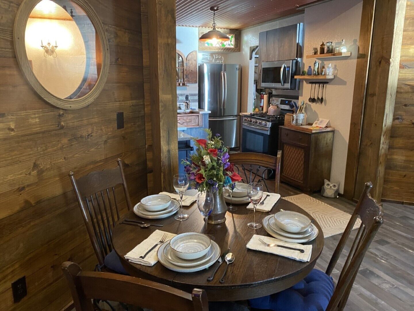 Een eetgedeelte met een ronde tafel voor vier personen, omringd door houten stoelen. Op de tafel staat een vaas met bloemen en er is uitzicht op een keuken op de achtergrond.