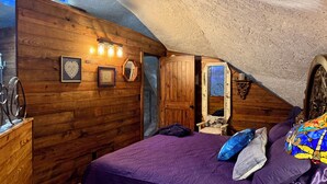 Ein Schlafzimmer mit Holzwänden, einer violetten Bettdecke und einem Spiegel mit dekorativem Rahmen.