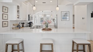 A spacious kitchen with white cabinetry, a large island with stools, pendant lighting, and artwork on the walls. - Seacrest Beach 30A | Lower Nightly Rates | My Beach Getaways (Seacrest Beach)