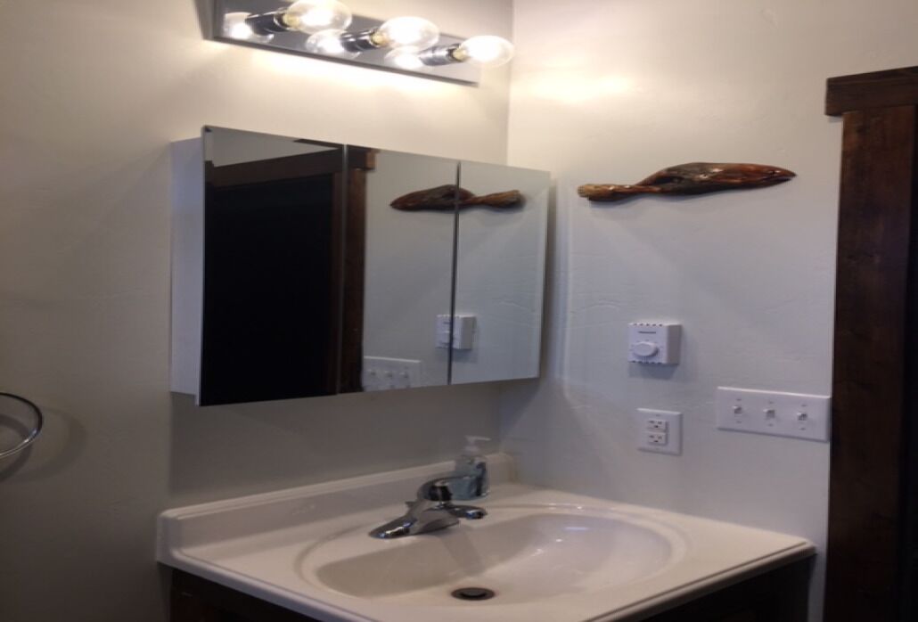 Un baño con un lavamanos blanco, un espejo encima y dos adornos de madera en la pared.