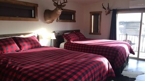 Quarto com duas camas, roupa de cama xadrez vermelha e preta, cabeceiras de madeira e cabeças de animais montadas nas paredes.