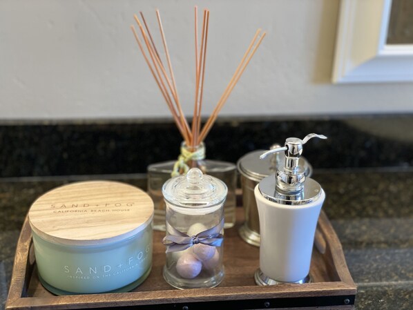 A wooden tray with a scented candle, a glass jar with a ribbon, and a white bottle with a pump.