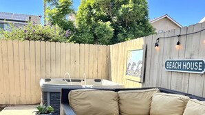 An outdoor patio with a fire pit, a beige sofa, and a hot tub.