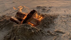 A beach scene with a dog, a fire pit, and the sun setting in the background.