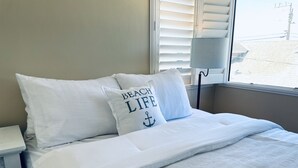 A neatly made bed with white bedding and pillows, including one with "BEACH LIFE" text.