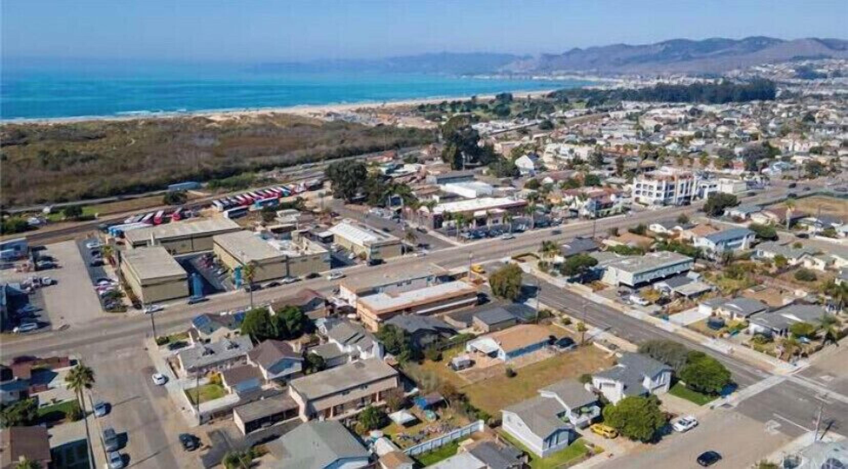 An aerial view of a coastal town with residential areas, a parking lot, and a beach in the background.