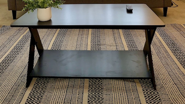 Una sala de estar con un sofá marrón, cojines blancos y marrones, una mesa de centro negra con una planta en maceta y una lámpara de pie.
