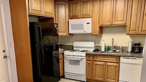 Una cocina con armarios de madera, un refrigerador negro, un microondas blanco, una estufa y un lavavajillas.