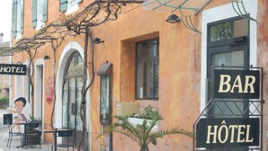 A building with signs for a hotel and a bar, outdoor seating, and a potted plant. - Modern holiday home with heated pool (Pradons)