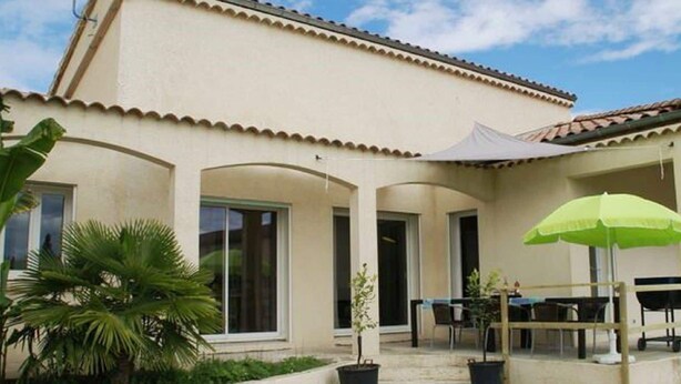 A building with a tiled roof, a covered patio area with a table and chairs, and potted plants. - Modern holiday home with heated pool (Pradons)