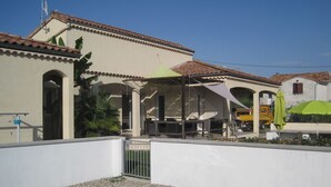 A pool area with a clear view of the pool, a covered patio, and a building with a tiled roof. - Modern holiday home with heated pool (Pradons)