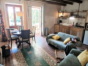 A cozy living room with a sofa, chairs, a dining table, and a kitchen area with cabinets and a sink.