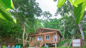 Ein Holzhaus mit einer Terrasse, umgeben von üppiger Vegetation und Bäumen.