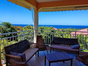 A balcony with a view of the ocean, featuring wooden furniture and a tiled floor. - FLAMBOYANT (3 - 8 people under 12 years old) (DESHAIES)