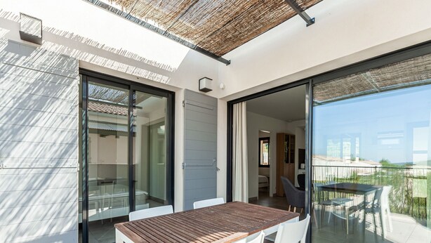 A modern outdoor dining area with a wooden table and white chairs, large sliding glass doors leading to a balcony with a view of the city. - Attractive Holiday Home in Malaucène with Terrace (malaucène)