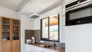 A modern kitchen with a built-in oven, a coffee maker, and a window with a view of the outdoors. - Attractive Holiday Home in Malaucène with Terrace (malaucène)
