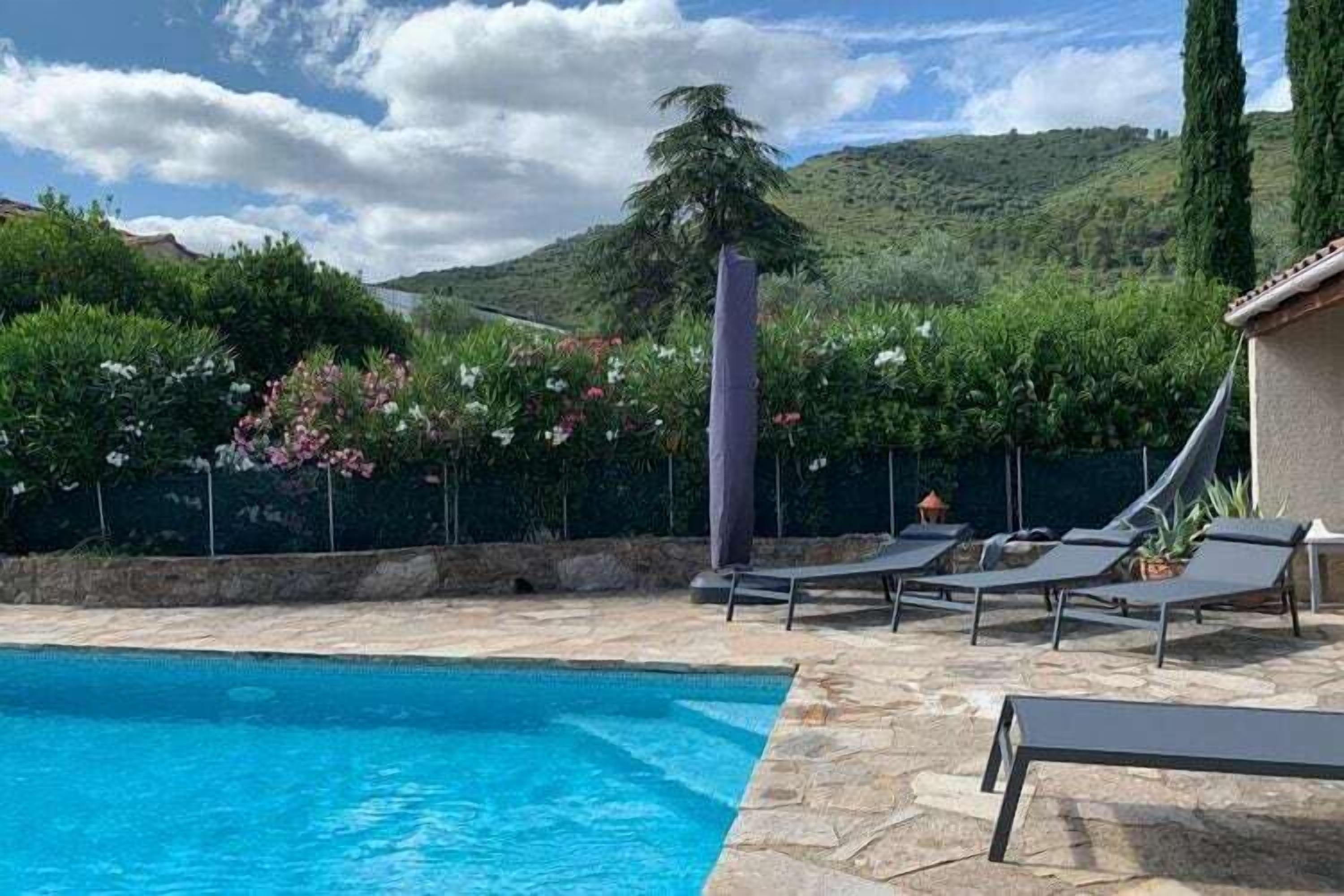 A swimming pool with lounge chairs and a pergola, surrounded by greenery and hills.