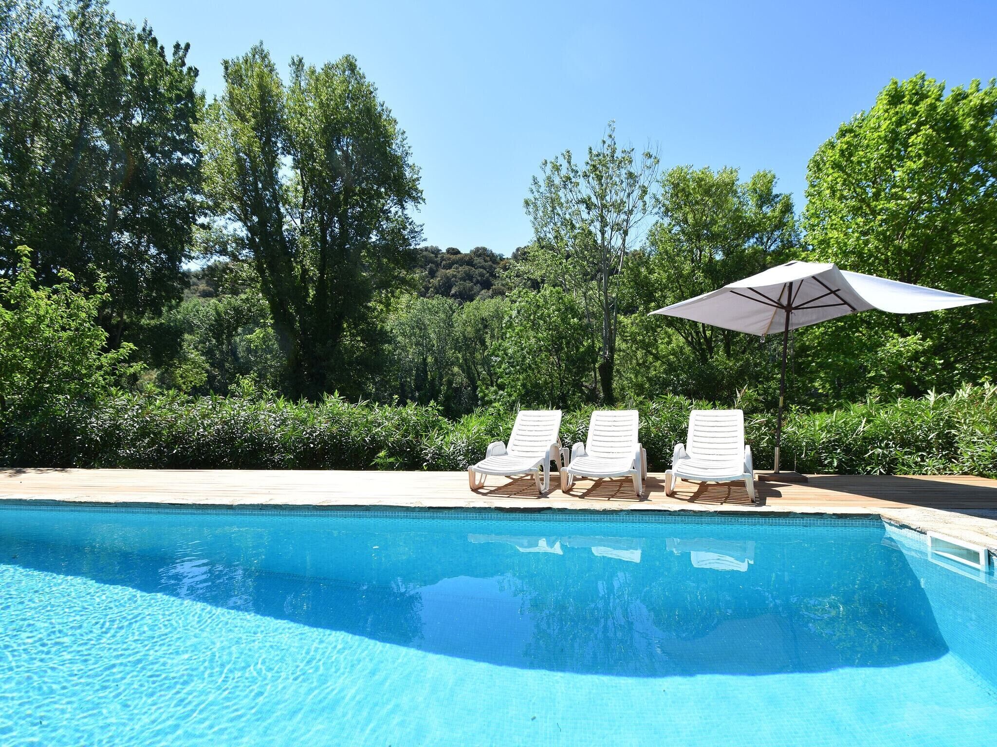 A clear blue pool with three white lounge chairs and a white umbrella.