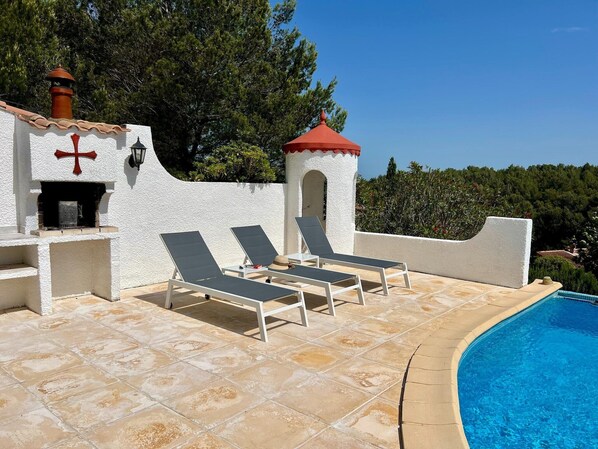 A poolside area with lounge chairs, a barbecue grill, and a small tower structure.
