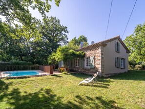 Una casa amb piscina, envoltada d'un jardí amb gespa i arbres.