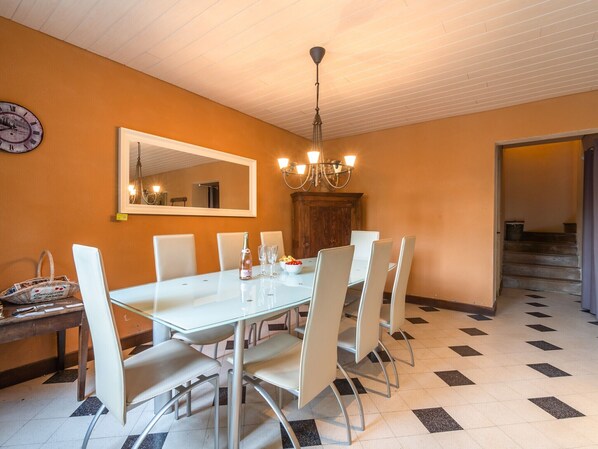 A dining area with a white table, six chairs, a chandelier, a wooden cabinet, and a clock on the wall.