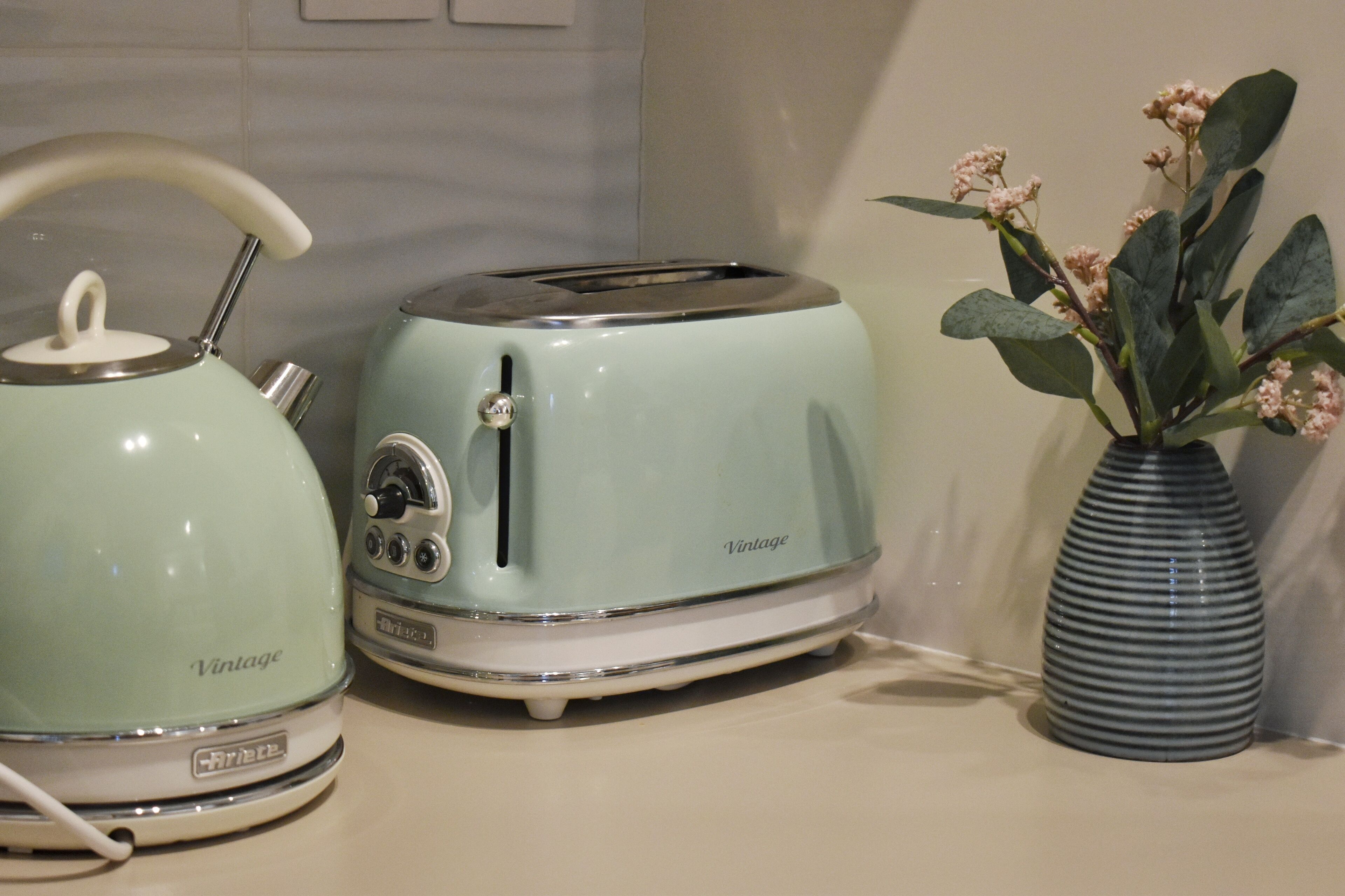 Retrotyylinen leivänpaahdin ja vedenkeitin keittiön työtasolla, maljakon vieressä, jossa on kukkia.