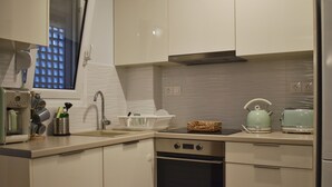 A modern kitchen with white cabinets, a stainless steel oven, a sink, and a window with a view of buildings. - Window to Acropolis (Athens)