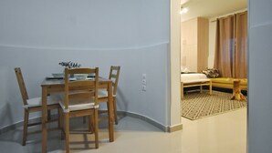 A room with a dining table and chairs, a bed with a patterned rug, and a sofa with curtains. - Window to Acropolis (Athens)