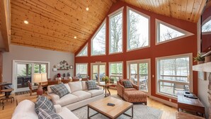 A spacious living room with a high ceiling, large windows, and a cozy seating area. - Stylish Lakefront Home w/ Foosball & Hot Tub (Oakland)