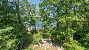 A forested area with a clear view of a lake and a small dock. - Stylish Lakefront Home w/ Foosball & Hot Tub (Oakland)
