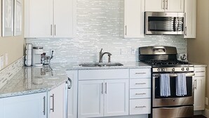 Una cocina moderna con gabinetes blancos, una estufa de acero inoxidable, un microondas y un salpicadero de azulejos.