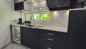 A modern kitchen with dark cabinetry, a white countertop, and a window with a view of greenery. - Studio Master   Residence Adam et  Eve (Baie Orientale)