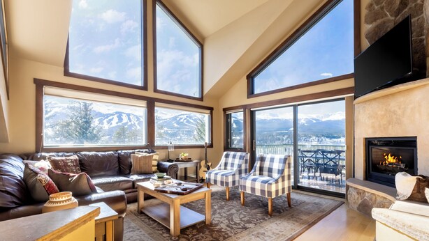 Un salón amplio con un gran ventanal con vistas a un paisaje montañoso, una chimenea y una zona de estar acogedora.