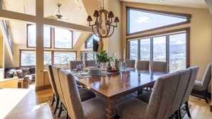 Un comedor amplio con una gran mesa de madera, varias sillas y un candelabro. La habitación cuenta con ventanas amplias que ofrecen vistas a la montaña.