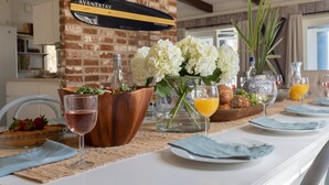 A breakfast setting with a wooden table, white flowers, and a brick wall with a sign. - Steps to Beach + Historic Cottage | Primary Balcony + Hammock | Sandpiper (Hilton Head Island)