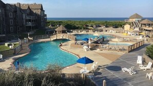 Un resort con varias piscinas, una terraza de madera y vista al océano.