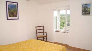 Ein Zimmer mit einem Bett, einem Sessel, einem Fenster mit Aussicht und zwei gerahmten Bildern an der Wand.