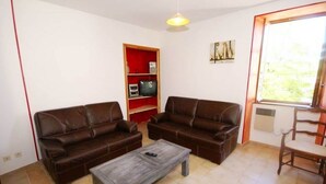 Ein Wohnzimmer mit zwei braunen Ledersofas, einem Holztisch, einer roten Unterhaltungsanlage mit Fernseher und einem Fenster mit Blick auf Grünflächen.